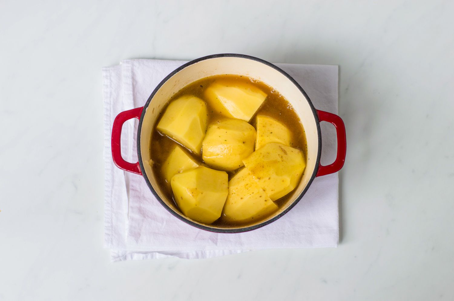 Scottish stovies in a Dutch oven with stock poured over potatoes