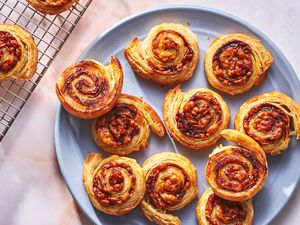 A blue plate with cheesy marmite puff pastry snails, with a wire rack with more snails