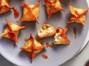 Several deep fried crab rangoons on a circular plate, one of them broken open so you can see the crab and cream cheese filling