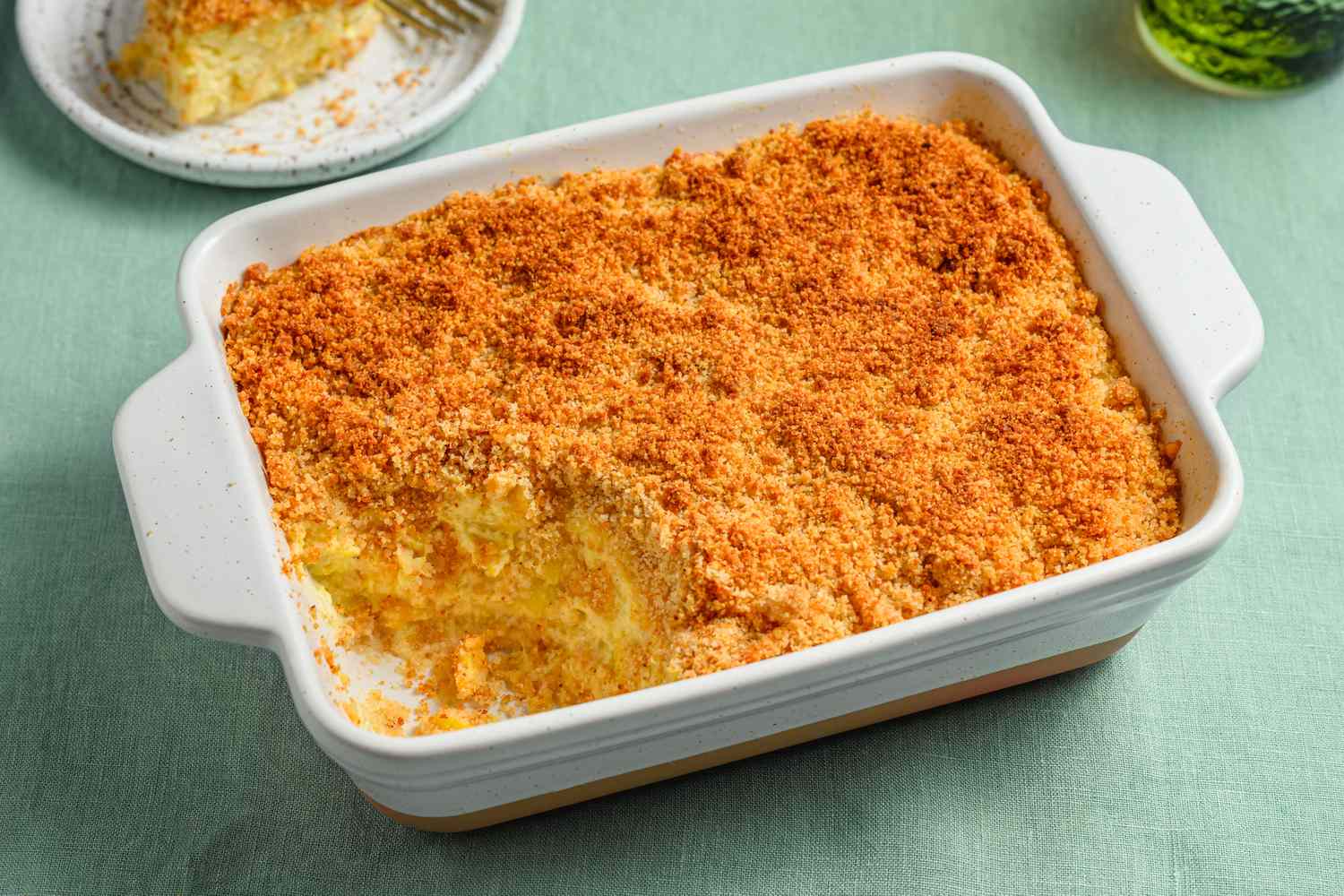 A yellow squash casserole in a large backing dish, with a plated portion of casserole