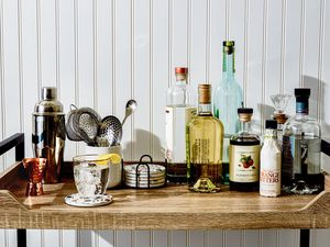 A well stocked bar cart with bar tools, liquor, and a sparkling cocktail garnished with a lemon peel