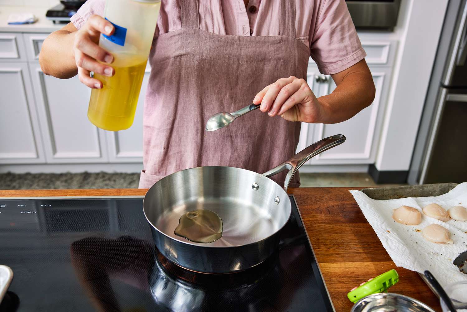 Person pouring oil into a pan from the Anolon Nouvelle Stainless 10-Piece Cookware Set