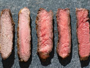 Five pieces of steak ranging from well-done to rare laid out on a slate surface