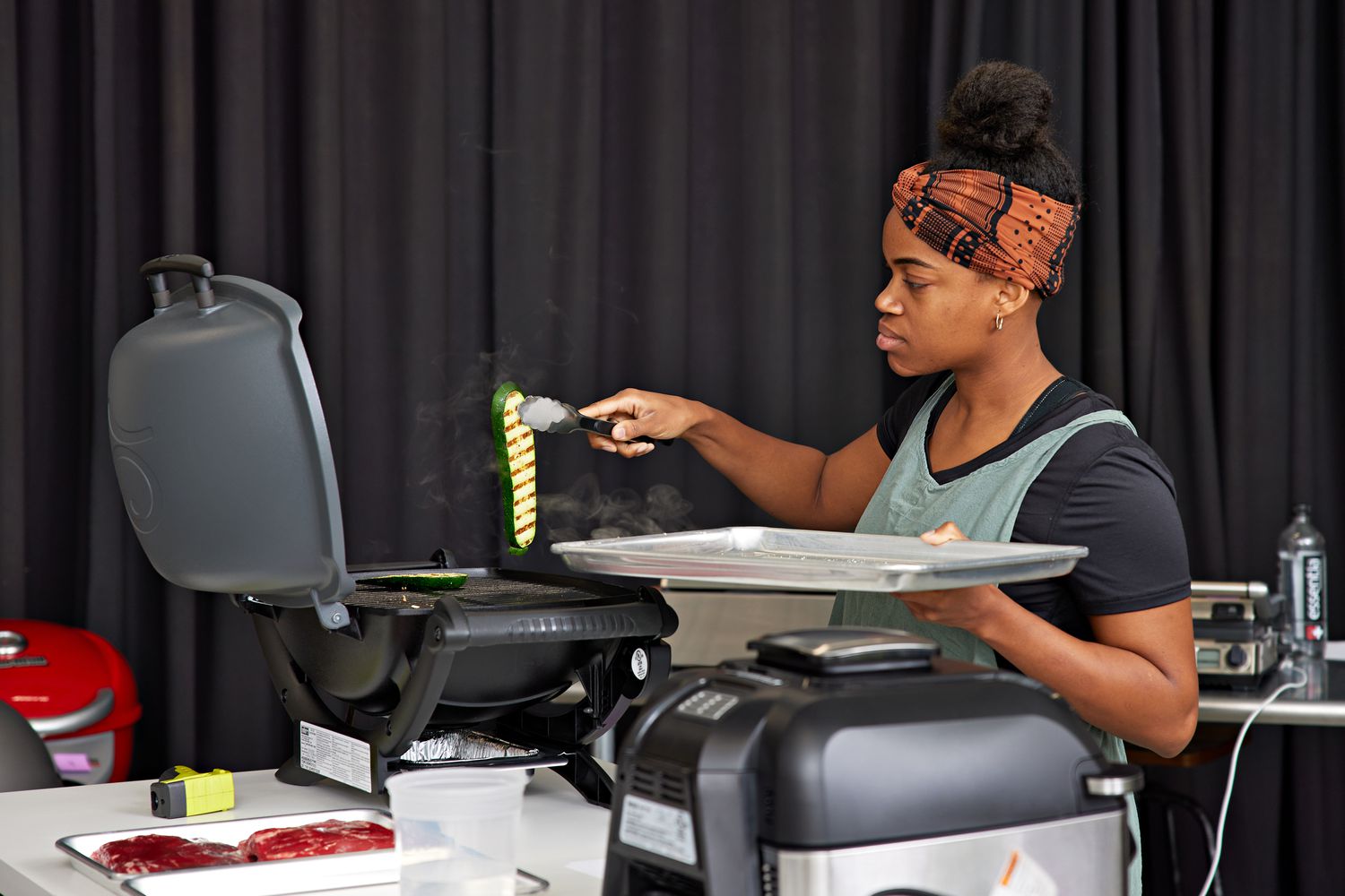 Woman using tongs to pick up a slice of zucchini from the Weber Q 1400 Electric Grill