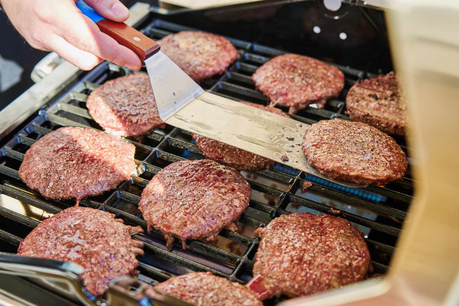 Hand using a spatula to flip burgers on the Char-Broil 463630021 Performance Series 2-Burner Gas Grill