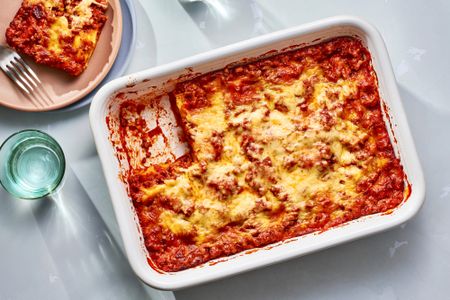 A ravioli lasagna in a baking dish, with a serving removed and served on a pink plate