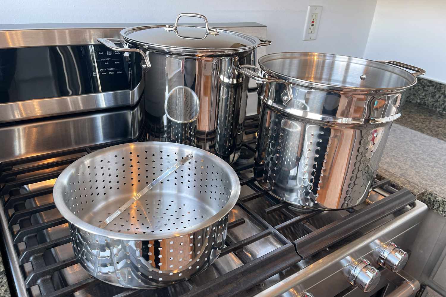 The All-Clad Gourmet Accessories Stainless Steel Multi-Pot with Perforated Steamer Insert and Lid, 12 Quart sits on a stovetop