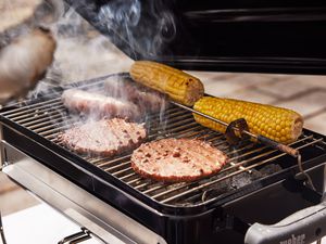 Burger patties, sausages and corn cooking on a Weber Go-Anywhere Charcoal Grill