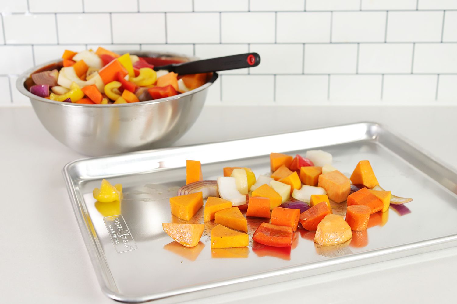 Nordic Ware Naturals Baker's Half Sheet with root vegetables and onion on a white counter