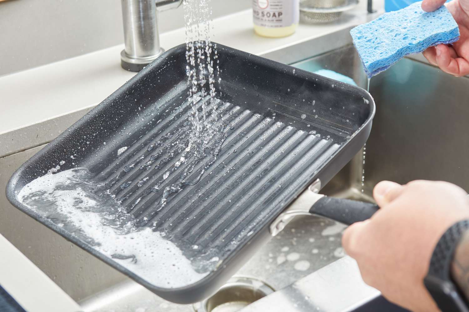 A person washing the OXO Good Grips 11” Square Grill Pan with soap and water. 
