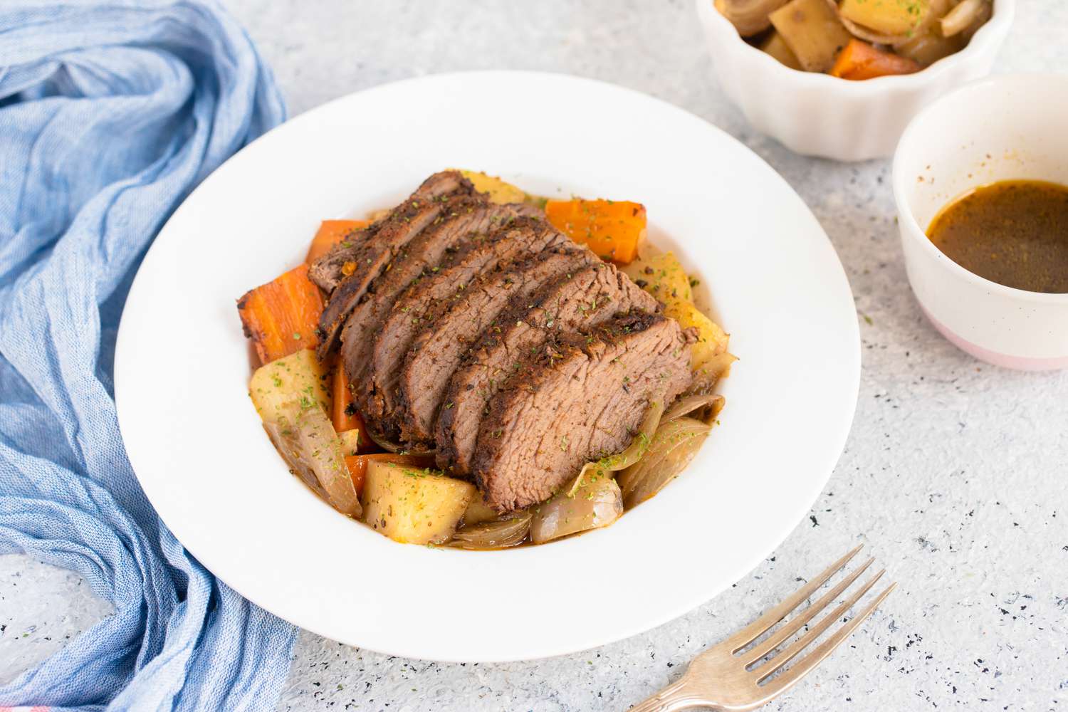 Thick slices of tri-tip roast with vegetables on a deep dinner plate next to a bowl with cooking liquids