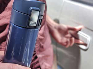 Hand holding Zojirushi Stainless Steel Mug while opening car door