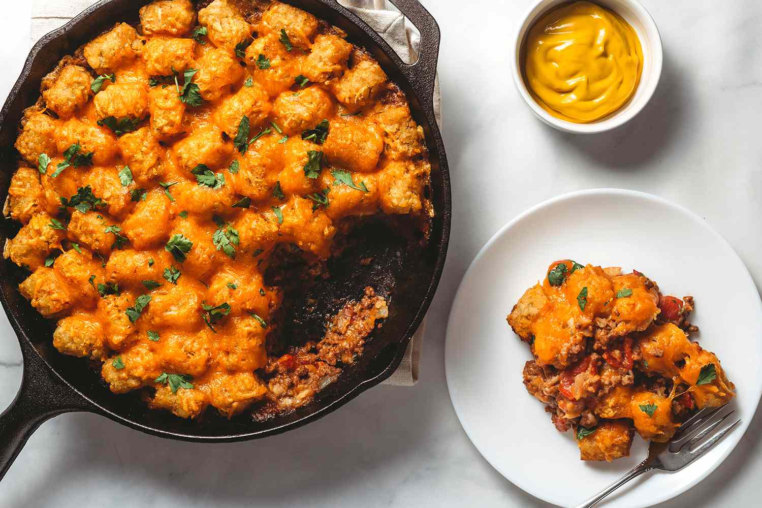 Cheeseburger Casserole in a cast iron skillet and on a plate, with a side of mustard