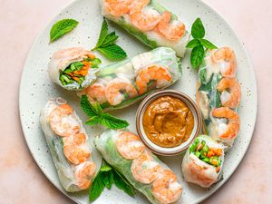A platter of Thai spring rolls with shrimp, served with a dipping sauce and topped with fresh mint