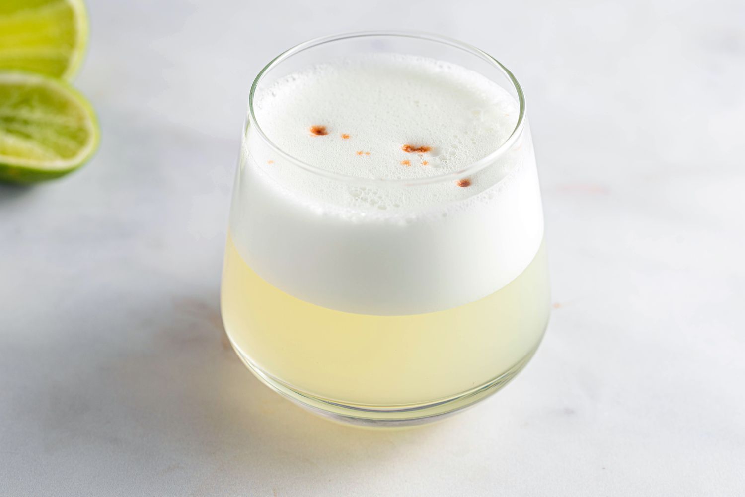 Peruvian pisco sour cocktail with foam on top and dashes of bitters in a tumbler