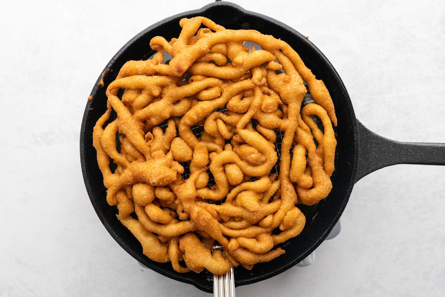 Golden-brown, puffed up funnel cake filling the skillet