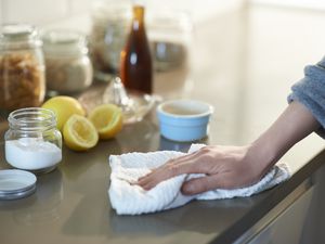 Person cleaning countertops with a cloth next to a container filled with baking soda and some lemons.