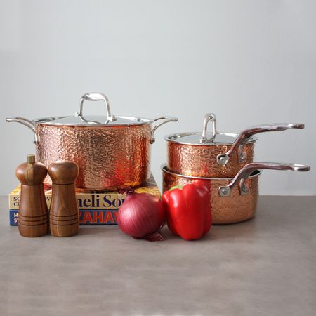 Lagostina Martellata 10-Piece Hammered Copper Cookware Set displayed on a beige surface next to a red pepper and onion