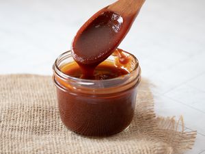Homemade barbecue sauce trailing off a wooden spoon into a small glass jar
