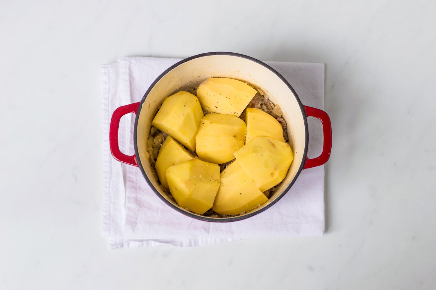 First potato layer in a Scottish stovies recipe in a Dutch oven