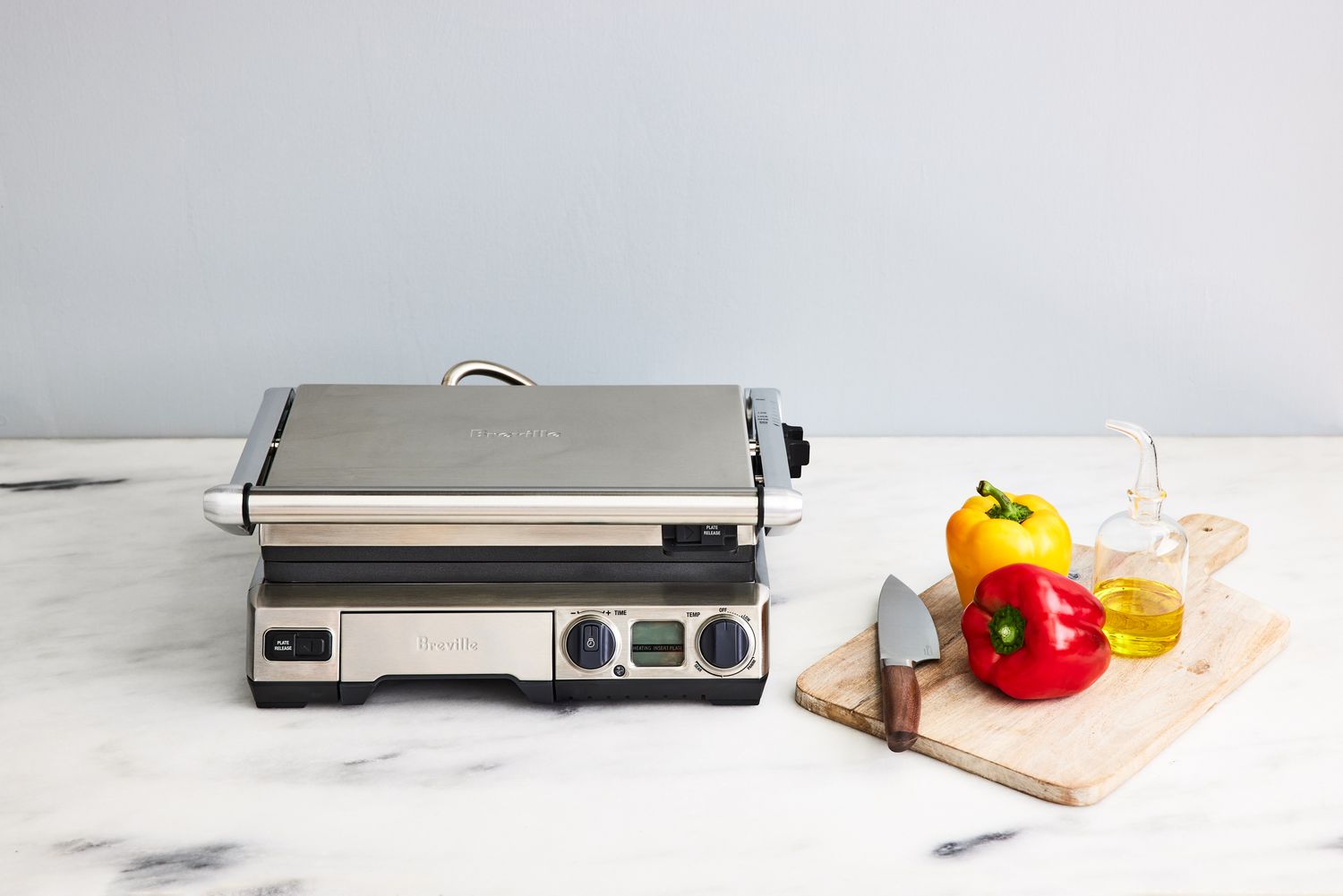 The Breville BGR820XL The Smart Grill on a counter next to a cutting board, peppers, a knife and oil