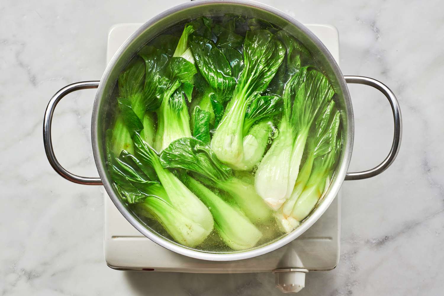 A pot of baby bok choy boiling in seasoned water