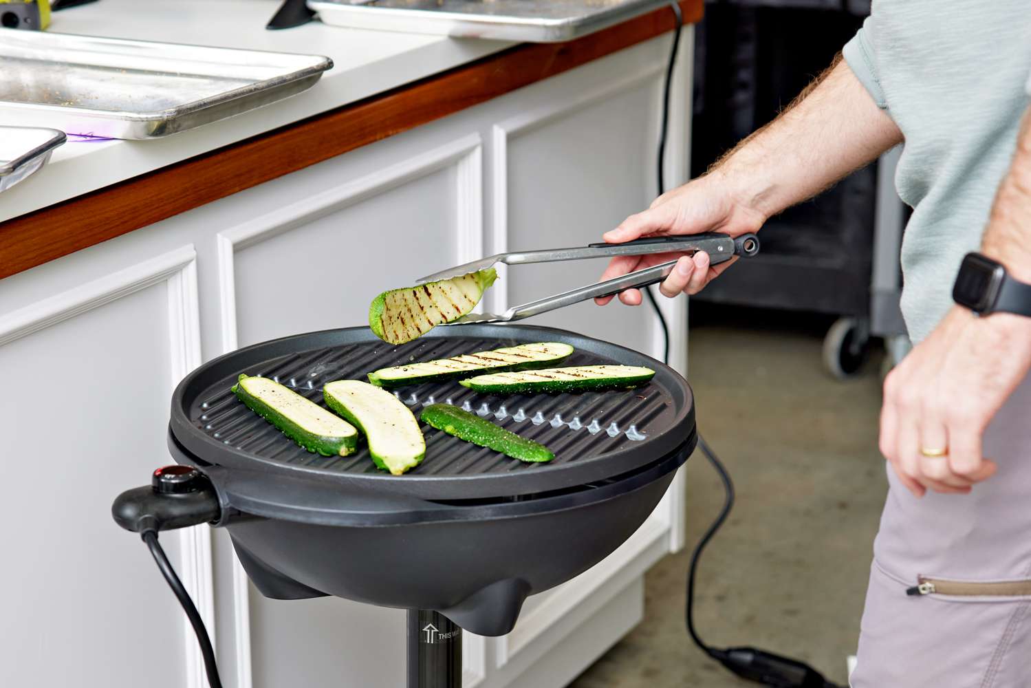 Person holding a slice of zucchini above a George Foreman GFO240S Indoor/Outdoor Electric Grill with slices of zucchini on top 