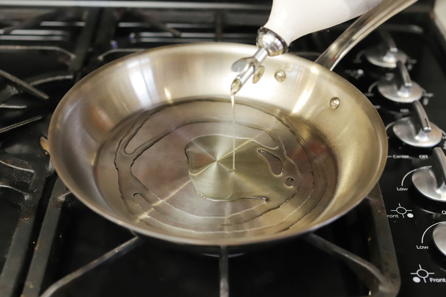 Drizzling oil into the All-Clad G5 frying pan on a gas stove