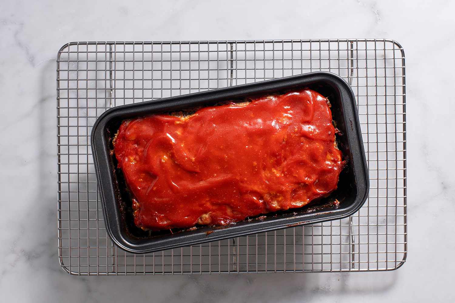 Baked meatloaf in a loaf pan on a metal wire cooling rack