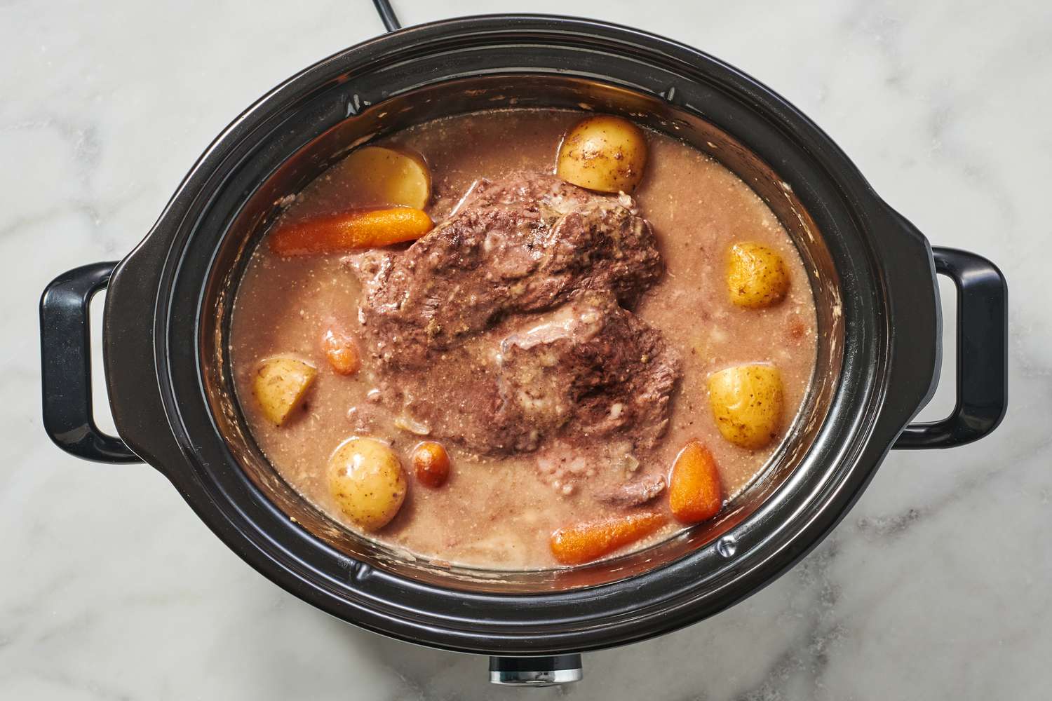 A slow cooker with a cooked onion soup beef pot roast with potatoes and carrots