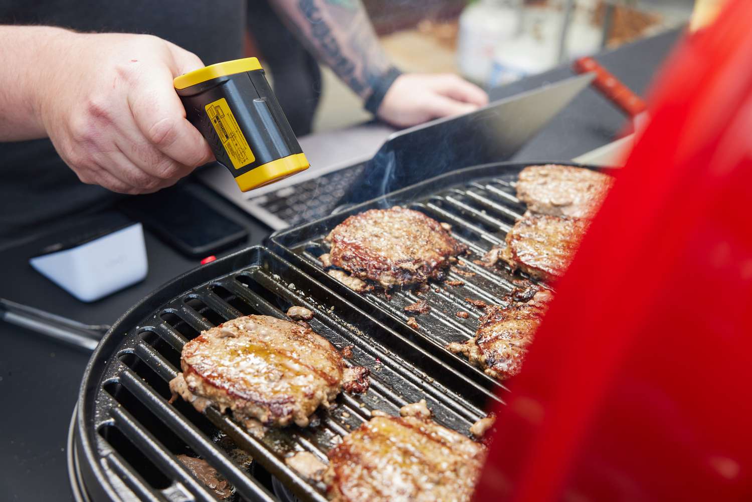 A man reads the temperature of grilling burgers on the Coleman Roadtrip portable grill