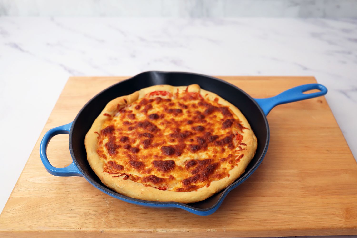Le Creuset Signature Skillet with pizza cooked inside on a wooden cutting board