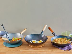 Three woks on a wooden table, holding stir-fry, fried eggs, and fried rice