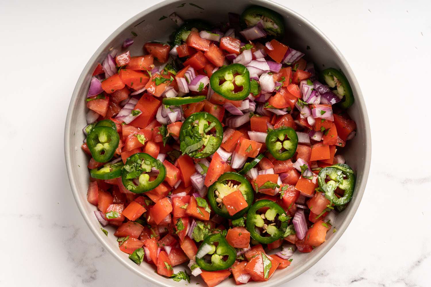Chopped onion, tomatoes, jalapeño pepper, and cilantro combined in a bowl 