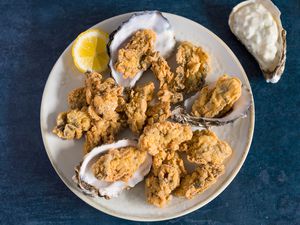 Crispy fried oysters with cornmeal batter on a plate with lemon wedge