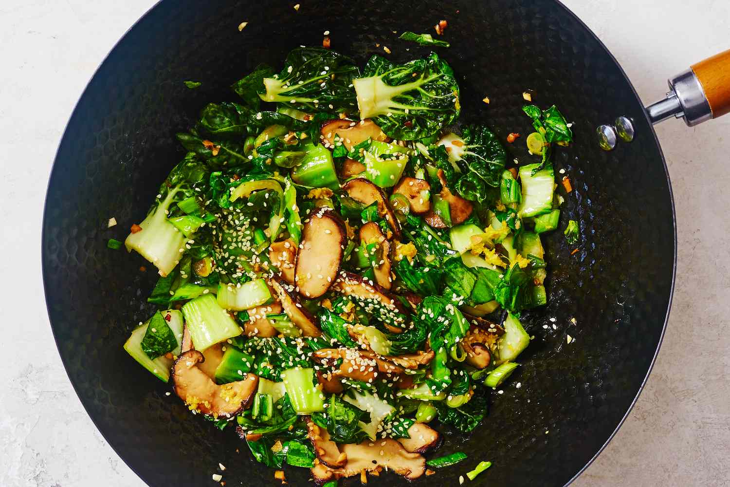 Bok choy and shiitake mushroom stir fry in a wok with sesame oil and seeds