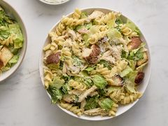 A large bowl of chicken caesar pasta salad, with a small serving in a bowl
