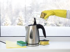 A person putting vinegar into a tea kettle in front of a window