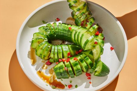 A bowl with spiral-cut cucumbers coiled inside, showing chopped hot red pepper as a garnish