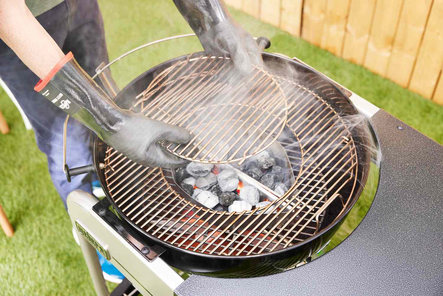 A tester places a grate above charcoals on the Weber Performer Deluxe