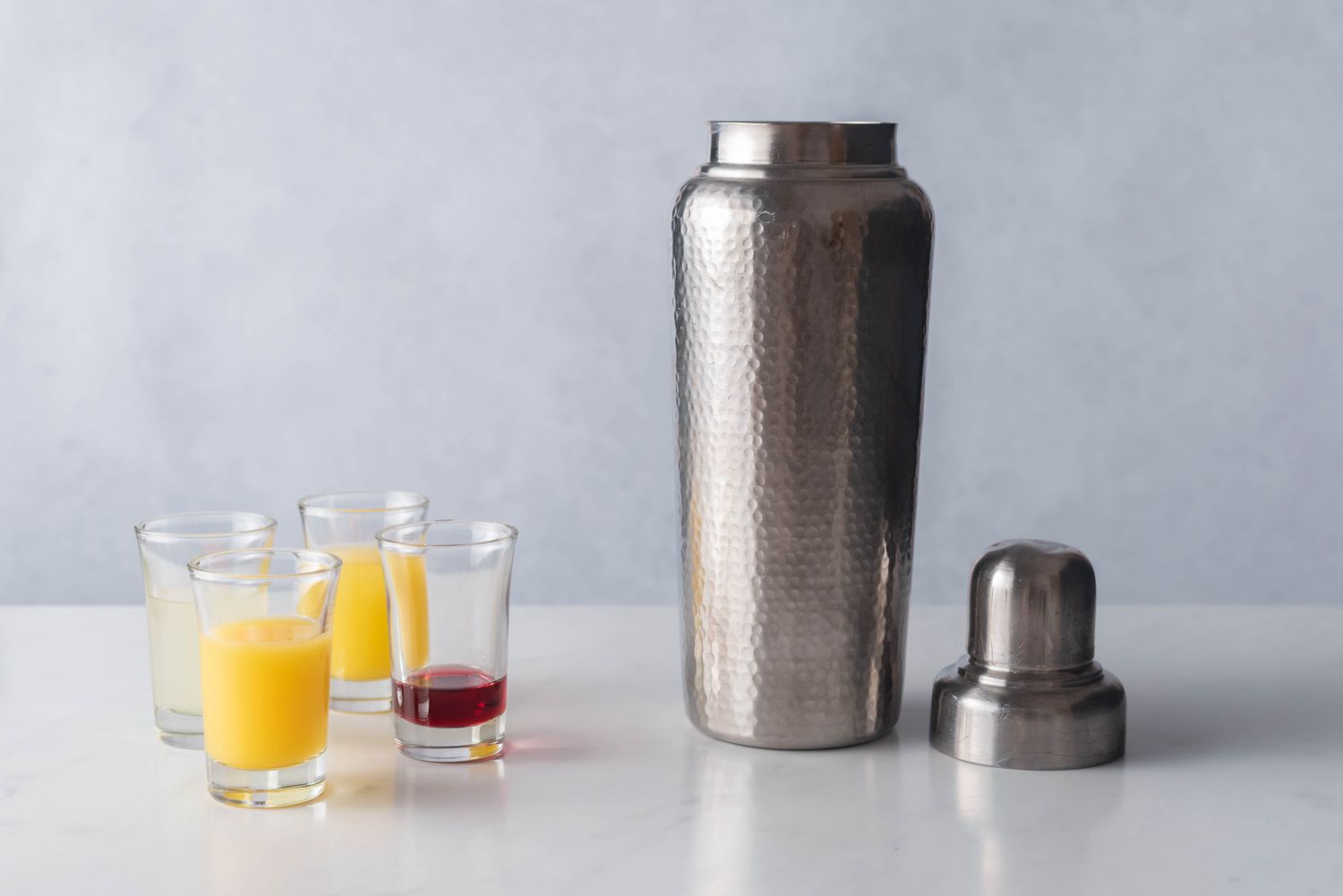 Juices and grenadine being poured into a metal cobbler-style shaker