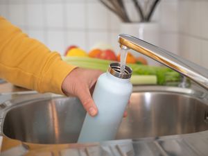 A person holding a blue water bottle next to a running faucet 