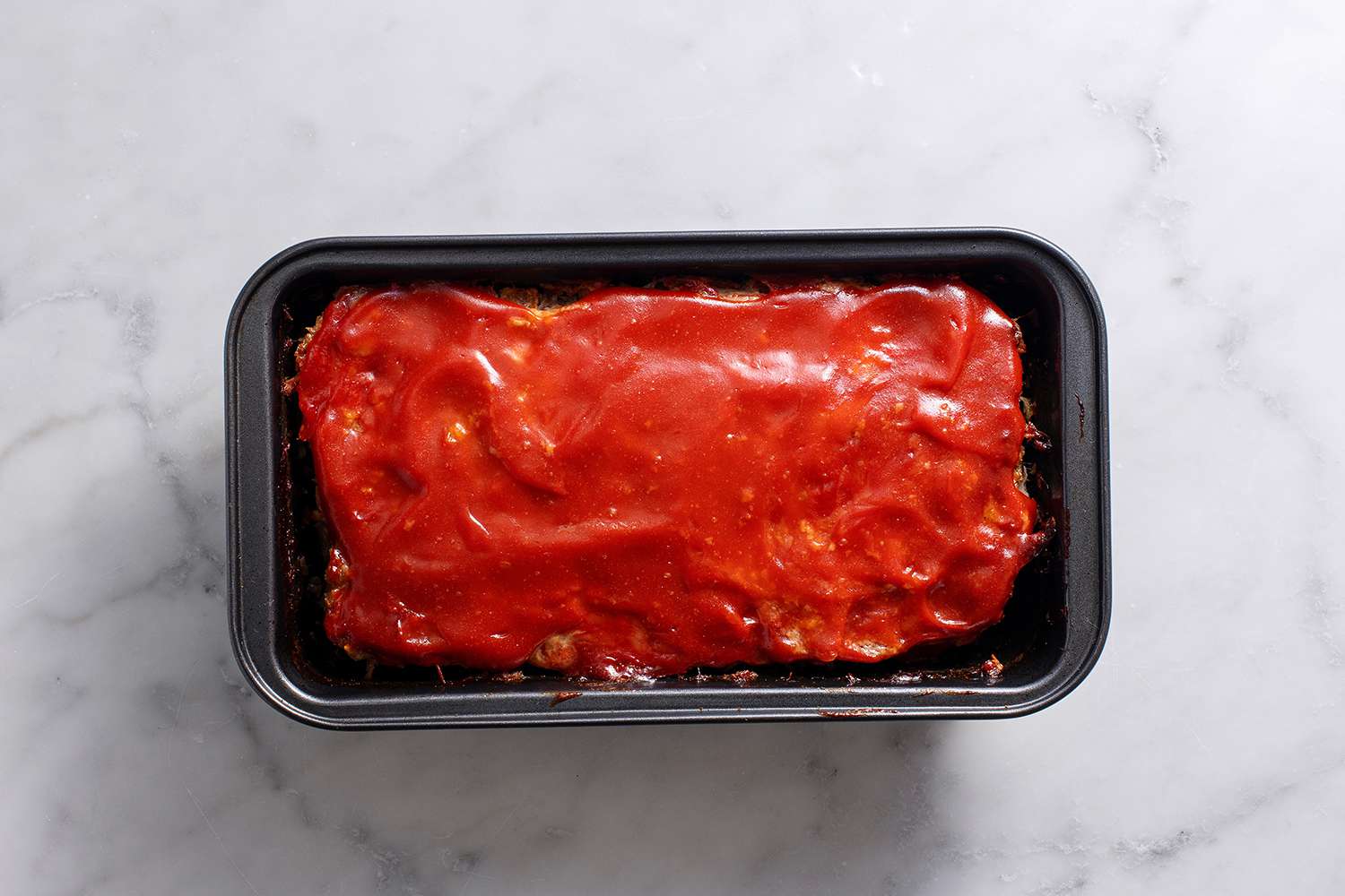 Baked meatloaf in a loaf pan evenly topped with more ketchup glaze