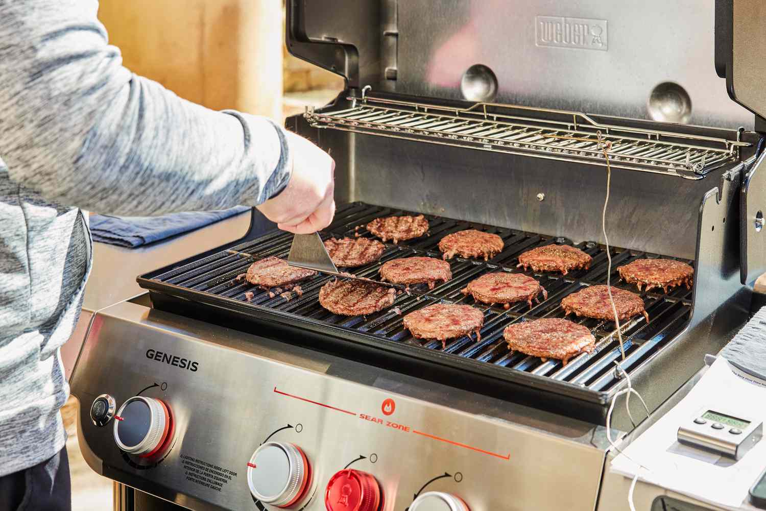 Person cooking burger patties on Weber Genesis EX-325S Propane Gas Smart Grill