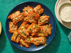 A round platter of parmesan smashed carrots topped with chopped parsley served with a small bowl of aioli