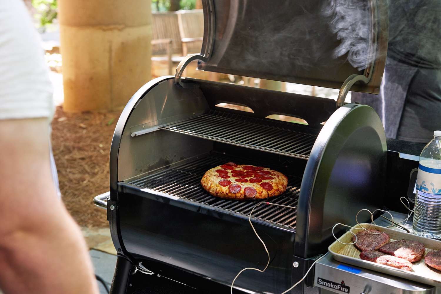 Person standing near Weber Smokefire EX4 (2nd Gen) Wood Fired Pellet Grill with a pizza inside it