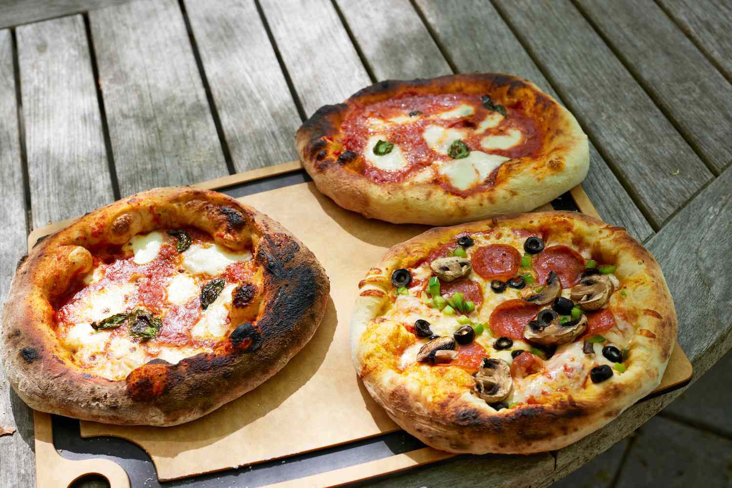 Three pizzas on a wooden board cooked in the Ooni Fyra 12 Portable Wood-Fired Outdoor Pizza Oven