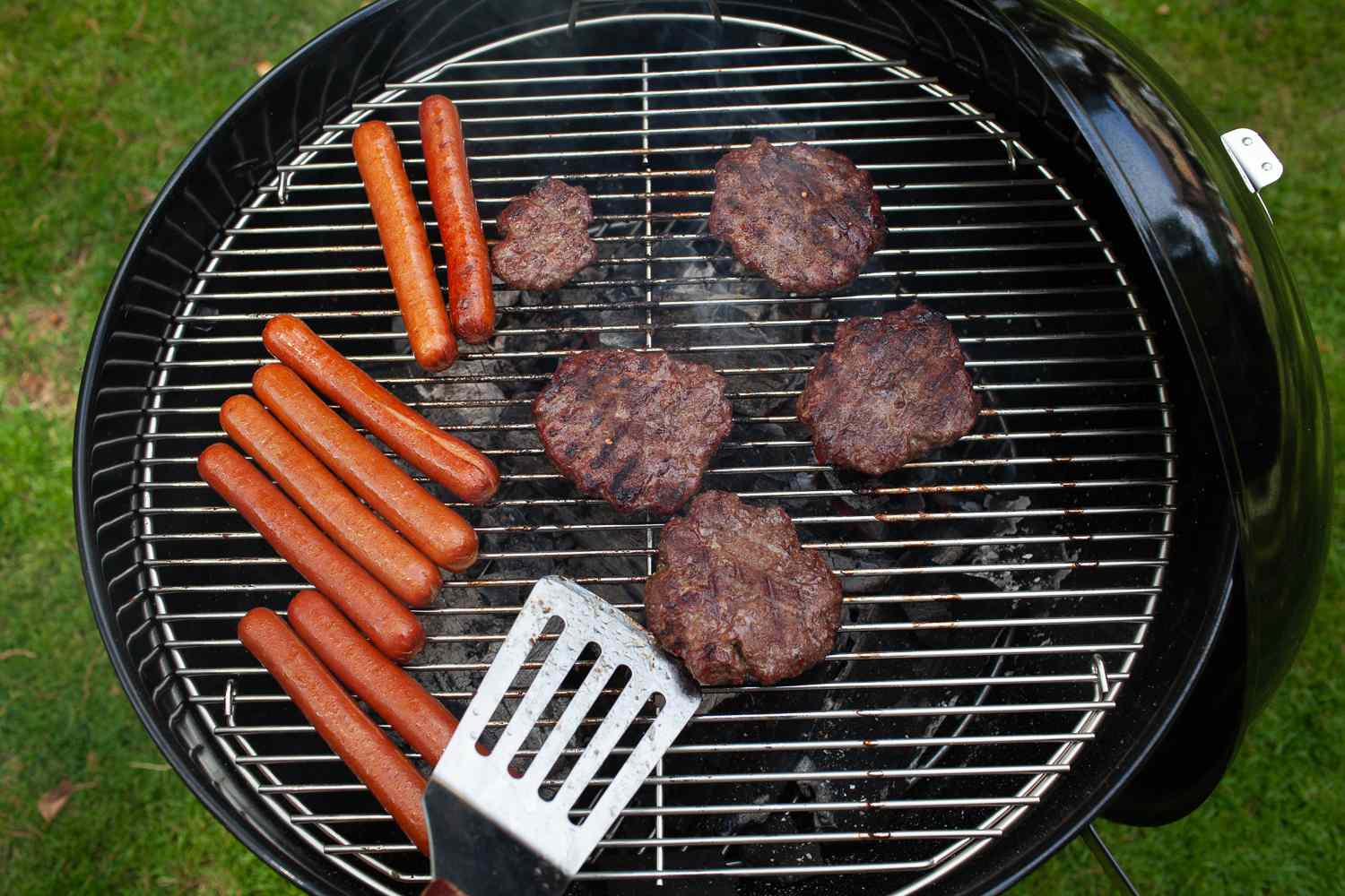 Weber Original Kettle Premium 22-inch Charcoal Grill with burgers and hot dogs on the grates