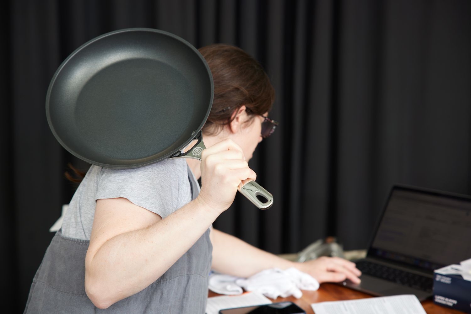 Person using a laptop holds the Le Creuset Toughened Nonstick Pro 6-Piece Cookware Set over their shoulder