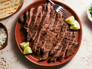 A red platter of sliced carne asada, served with lime wedges